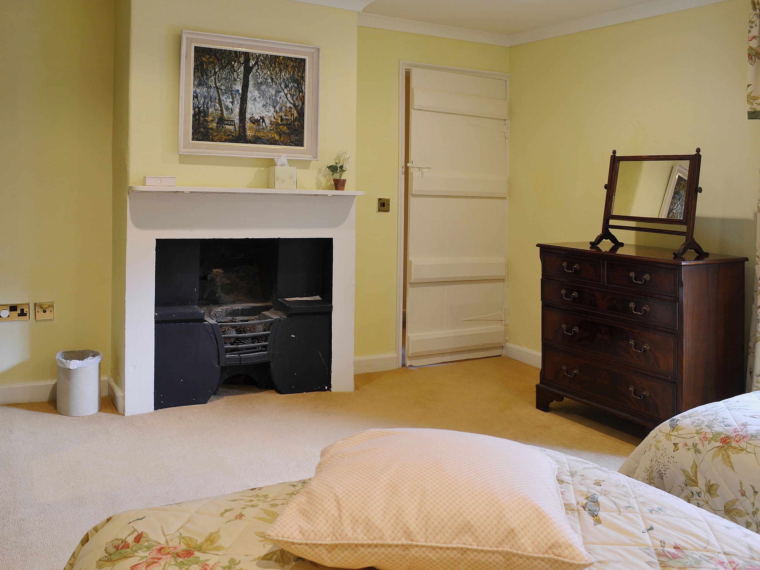 A bedroom with a fireplace, a dresser, a bed with floral bedding, and a painting on the wall.