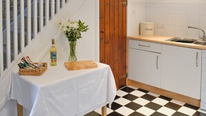 Une cuisine avec un carrelage à motifs, une porte en bois, un évier et une table sur laquelle se trouvent un vase de fleurs et une bouteille.