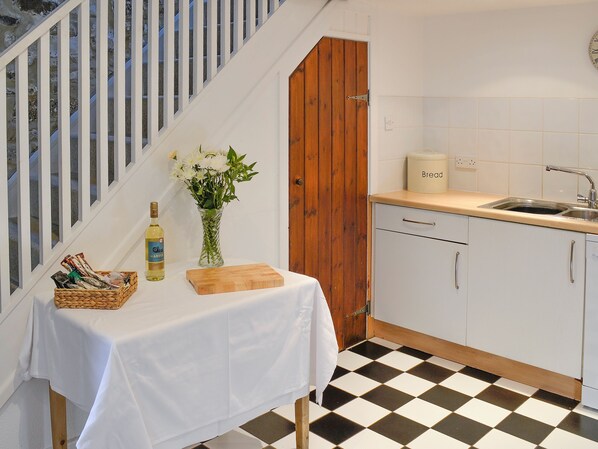 Een keuken met een zwart-witte vloer, een houten deur, een spoelbak en een tafel met een bloevas en een fles.
