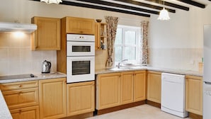 A kitchen with wooden cabinets, a double oven, a dishwasher, and a window with curtains.