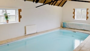 An indoor swimming pool with tiled walls, a wooden ceiling, and a window with a potted plant.