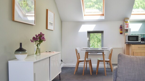 A compact kitchen with a dining area, featuring a white cabinet, a small table, and two chairs. There are skylights above the windows, and a microwave on the counter. - 1 bedroom accommodation in York (York)