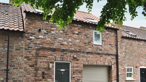 A brick building with a green door labeled "18", a garage door, and a small window. - 1 bedroom accommodation in York (York)
