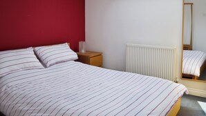 A bedroom with a sloped ceiling, a bed with striped bedding, a bedside table, a mirror, and a radiator. - 1 bedroom accommodation in York (York)