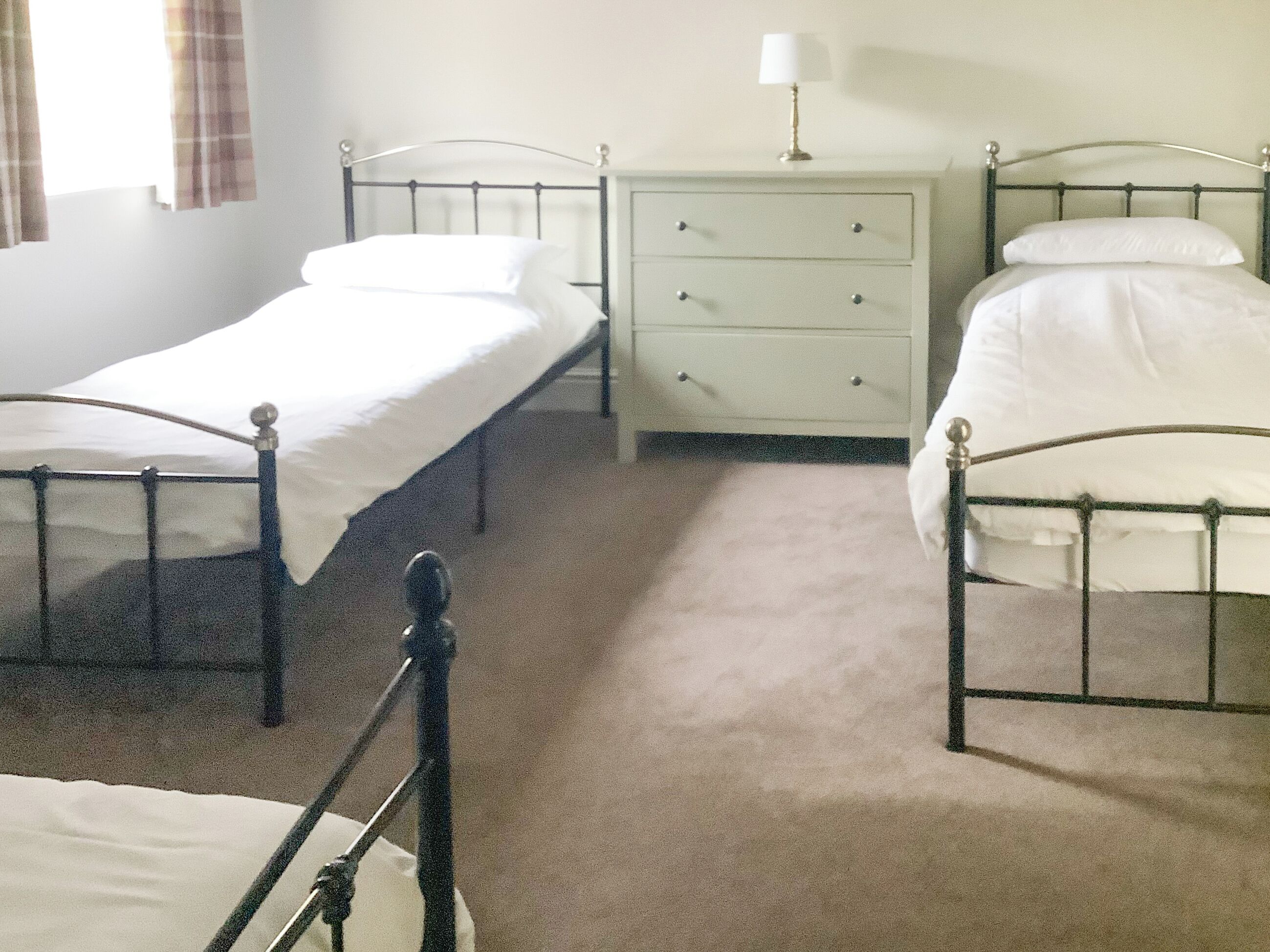 A bedroom with two single beds, a nightstand with a lamp, and a dresser.