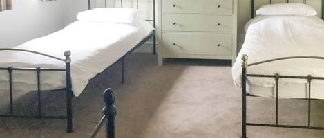 A bedroom with two single beds, a nightstand with a lamp, and a dresser.