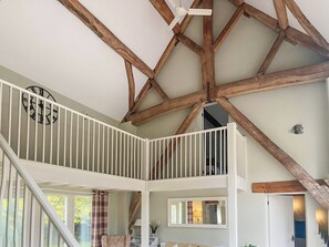 A multi-level interior with exposed wooden beams, a white railing, and a clock on the upper level.