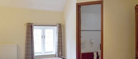 A bedroom with a bed, a window with curtains, a wooden door, and a bathroom visible through the door.