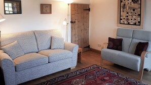 A living room with a grey sofa, a blue armchair, a patterned rug, and a wooden door. - 3 bedroom accommodation in Helton (Helton)