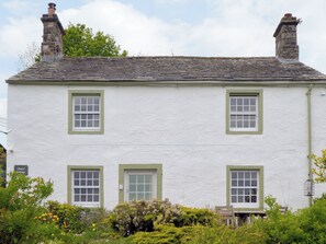 Um edifício de dois andares com fachada branca e molduras de janela verdes, uma chaminé e uma placa com a inscrição 'Chapel Cottage'.
