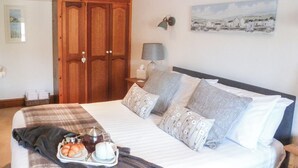 A neatly made bed with a tray of croissants and a cup of coffee, a wooden wardrobe, a lamp, and a painting on the wall. - 3 bedroom accommodation in Mevagissey, near St. Austell (Mevagissey, near St. Austell)