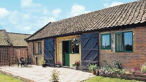 Ein Ziegelhaus mit einem Ziegeldach, einer Haustür und einer kleinen Terrasse mit Tisch und Stühlen.