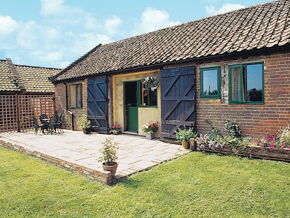 A brick house with a tiled roof, a front door, and a small patio area with a table and chairs.