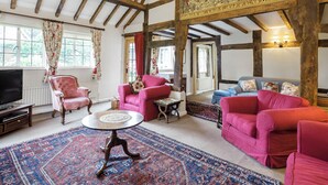A spacious room with exposed wooden beams, a large tapestry, and a mix of pink and blue sofas. - 3 bedroom accommodation in Bucknell, near Clun (Bucknell, near Clun)