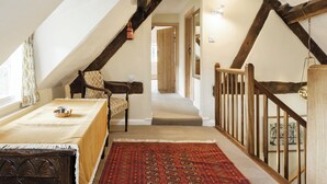 A cozy attic bedroom with a sloped ceiling, wooden beams, a bed with a patterned bedspread, a chair, and a red patterned rug. - 3 bedroom accommodation in Bucknell, near Clun (Bucknell, near Clun)