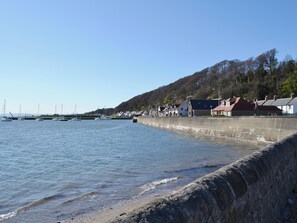Blick auf das Wasser mit vertäuten Booten, einer Steinmauer und Häusern entlang des Ufers.