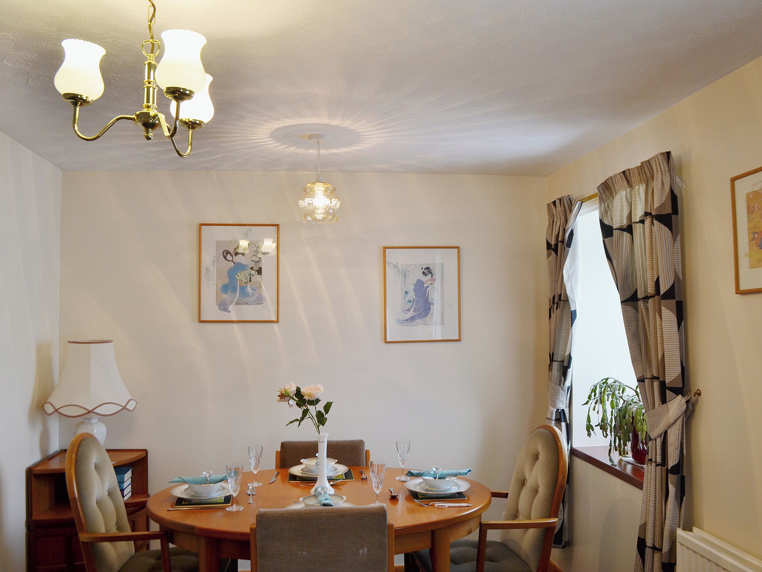 A dining area with a wooden table set for four, framed artwork on the walls, and a chandelier above.