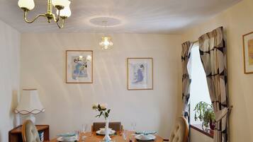 A dining area with a wooden table set for four, framed artwork on the walls, and a chandelier above.