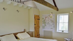Ein Schlafzimmer mit einem Bett, einer hölzernen Kommode, einem Heizkörper, einer Karte an der Wand und einem Fenster.