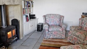Ein gemütliches Wohnzimmer mit Kamin, einer Bücherwand und Sesseln mit Blumenmuster.