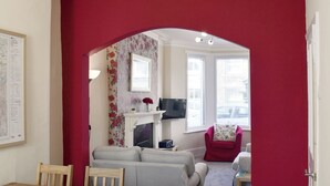 Una sala de estar con un arco rojo, un sofá gris, una mesa de comedor de madera y un televisor al fondo.