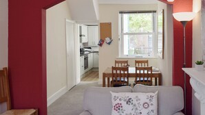 Un salón acogedor con sofá, una mesa de comedor con sillas, una cocina al fondo y una ventana con vistas.