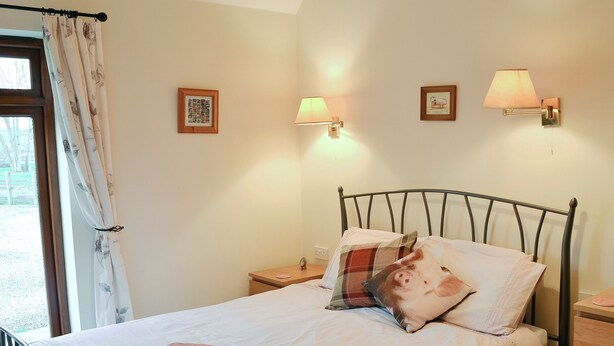 A neatly made bed with a rolled towel, a headboard, and two wall-mounted lamps. - 2 bedroom accommodation in East Tytherton, Chippenham (East Tytherton, Chippenham)