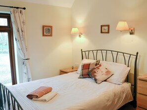 A neatly made bed with a rolled towel, a headboard, and two wall-mounted lamps.