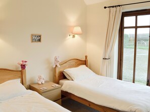 A bedroom with two beds, a nightstand, a lamp, a picture on the wall, and a view of the outdoors through a window. - 2 bedroom accommodation in East Tytherton, Chippenham (East Tytherton, Chippenham)