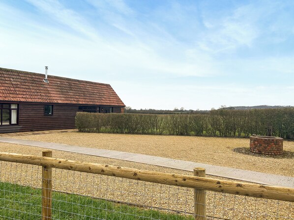 A rustic barn with a sloped roof, surrounded by a gravel path and a hedge.