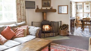 A cozy living room with a fireplace, a sofa with patterned cushions, a wooden table, and a dining area with chairs. - 4 bedroom accommodation in Newent, Forest of Dean (Newent, Forest of Dean)