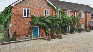 A brick building with a blue door, multiple windows, and a gravel driveway. - 4 bedroom accommodation in Newent, Forest of Dean (Newent, Forest of Dean)