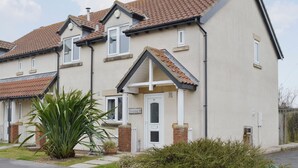 A two-story residential building with a tiled roof, a brick chimney, and a small garden with a palm plant. - Modern town house only a short distance from the centre of Seahouses. (Seahouses)