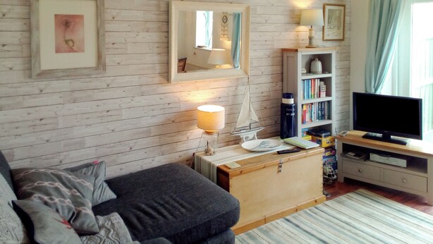 A cozy living room with a wooden wall, a sofa, a coffee table, a bookshelf, and a television. - Modern town house only a short distance from the centre of Seahouses. (Seahouses)