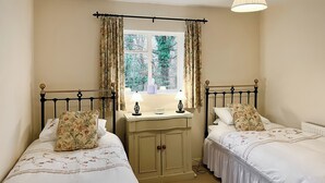 A bedroom with two single beds, a bedside table with a lamp, and a window with curtains. - 2 bedroom accommodation in Fressingfield (Fressingfield)