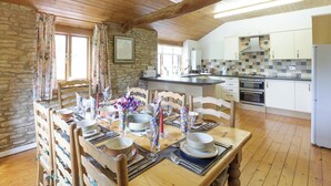 A cozy dining area with wooden furniture, a stone wall, and a kitchen in the background. - 4 bedroom accommodation in Lea, near Ross-on-Wye (Lea, near Ross-on-Wye)