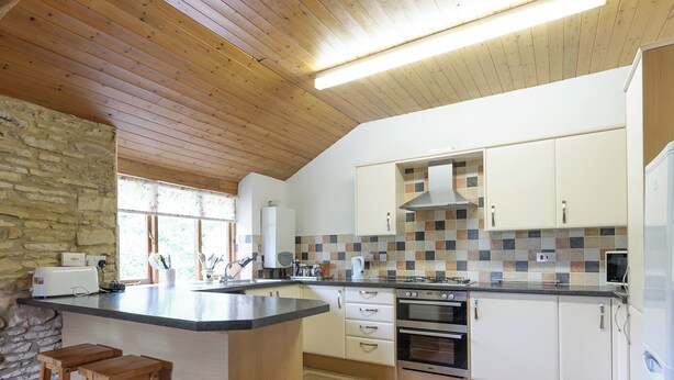 A modern kitchen with a wooden ceiling, stone wall, and a tiled backsplash. - 4 bedroom accommodation in Lea, near Ross-on-Wye (Lea, near Ross-on-Wye)