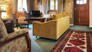 A cozy living room with a sofa, armchair, and a television on a wooden table. - 4 bedroom accommodation in Lea, near Ross-on-Wye (Lea, near Ross-on-Wye)