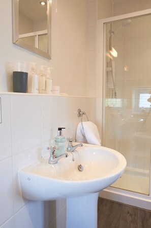 A bathroom with a white sink, a mirror, and a glass-enclosed shower. - Corner Beech House (Grange-over-Sands)