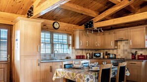A wooden kitchen with a dining table set for four, a clock, and a window with blinds. - Lake View Lodges - 25076 (Old Leake, near Boston)