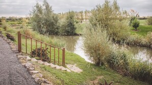 A gravel path leading to a wooden fence beside a calm river, surrounded by lush greenery and trees. - Lake View Lodges - 25076 (Old Leake, near Boston)