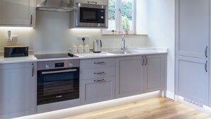 A modern kitchen with grey cabinetry, a built-in oven, a microwave, and a window above the sink.