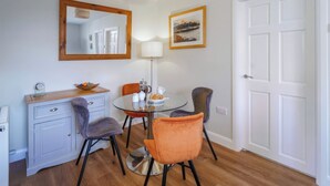 A compact dining area with a round glass table, two chairs, a small cabinet, and a mirror above the table.