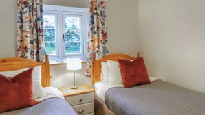 A double room with two beds, a wooden headboard, a bedside table with a lamp, and a window with floral curtains.