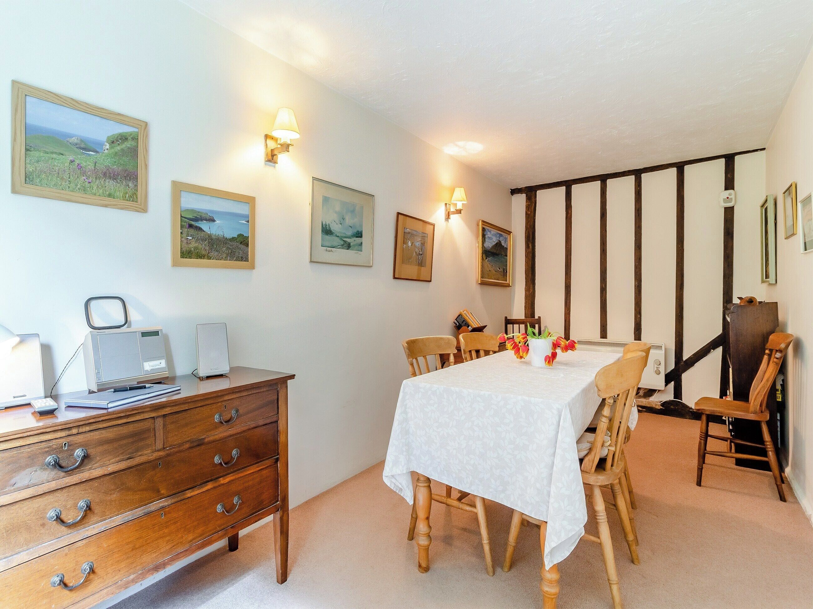 Un coin repas avec une table dressée pour quatre personnes, des chaises en bois, une commode en bois avec des tiroirs et des œuvres d’art accrochées au mur.