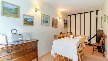 Un coin repas avec une table dressée pour quatre personnes, des chaises en bois, une commode en bois avec des tiroirs et des œuvres d’art accrochées au mur.