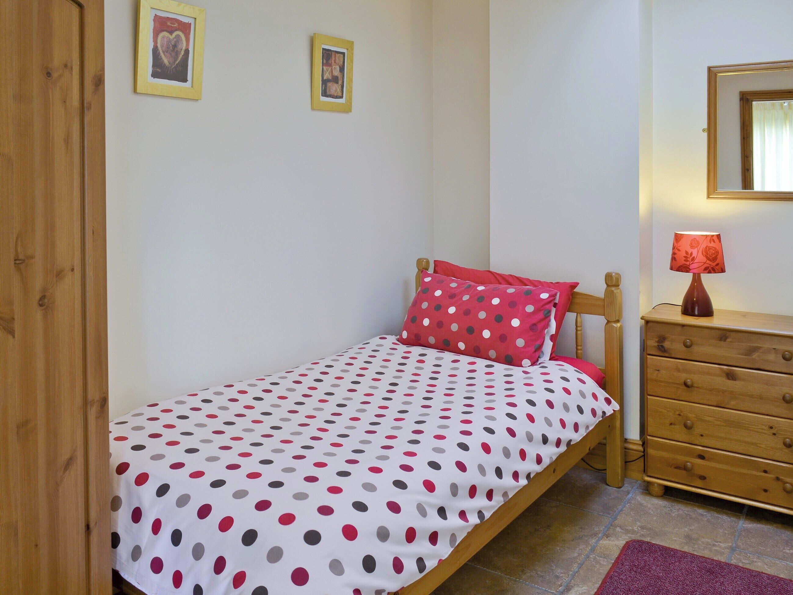 A bedroom with a bed, a dresser, a lamp, and two framed pictures on the wall.