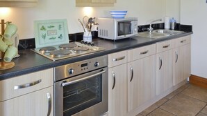 A modern kitchen with stainless steel appliances, wooden cabinets, and a tiled backsplash. - SWALLOWS COTTAGE - 24285 (Filey)