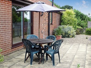 A patio with a brick wall, a glass door, and a table with chairs under a large umbrella.