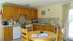 A kitchen with wooden cabinets, a tiled backsplash, a dining table with chairs, and a view of the outdoors through a window. - 2 bedroom accommodation in Leiston, near Aldeburgh (Leiston, near Aldeburgh)